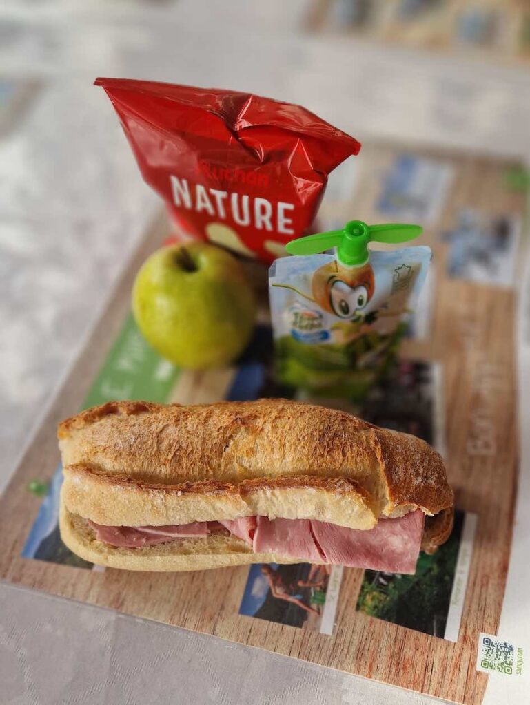 Panier pique-nique par Jeanne composé d'un sandwich jambon/fromage, d'un fruit, d'une compote et d'un paquet de chips